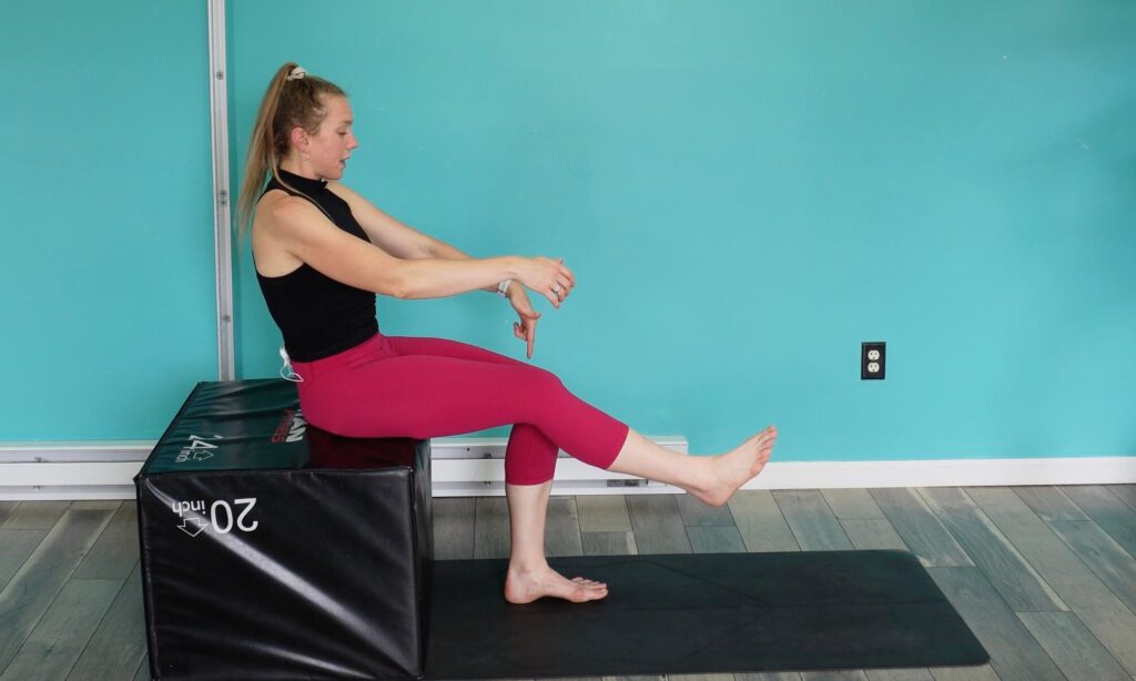 Dr. Chloe seated on a box with 1 leg elevated in front of her after doing the eccentric chair squat for knee strengthening